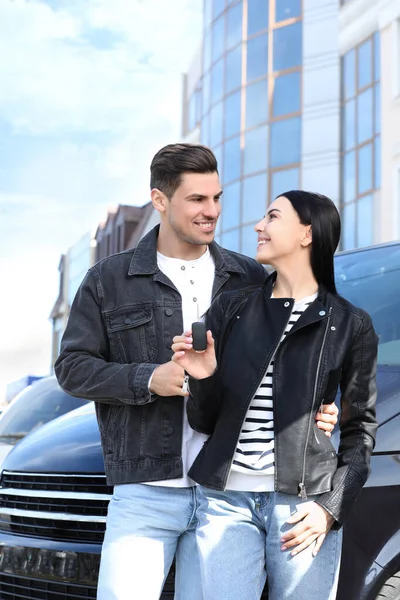 Happy couple with key near car on city street. Buying new auto