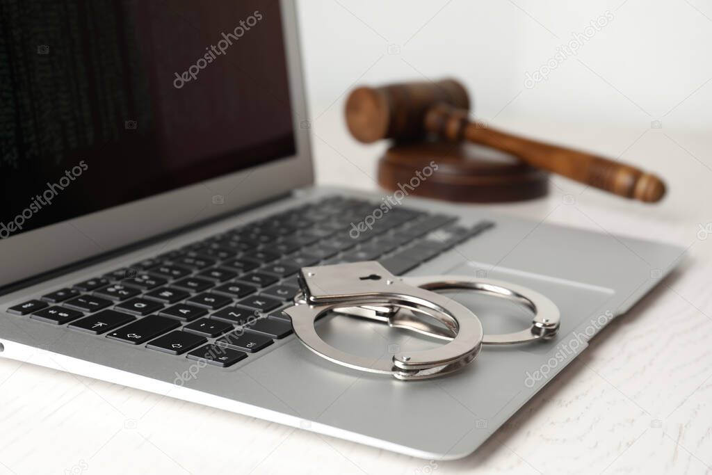 Laptop, gavel and handcuffs on white table, closeup. Cyber crime