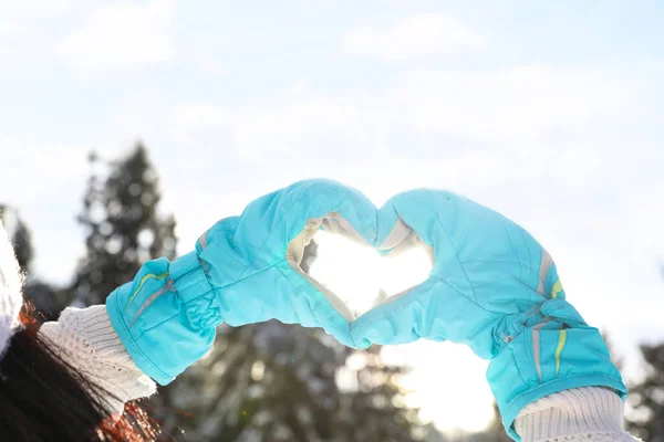 Young woman making heart with hands outdoors, closeup. Winter vacation