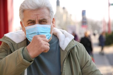 Şehir caddesinde tıbbi maskeli yaşlı bir adam öksürüyor. Virüs koruması
