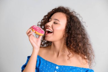 Açık gri arka planda donutu olan güzel Afro-Amerikalı kadın.