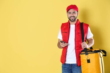 Sarı arka planda termal çantalı ve cep telefonlu kurye. Mesaj için yer var. Yemek dağıtım servisi.