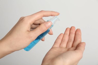 Açık gri arka plana antiseptik jel süren kadın, yakın plan.