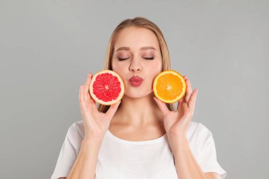 Gri arka planı kesilmiş turuncu ve greyfurtlu genç bir kadın. Vitamin zengini yiyecekler
