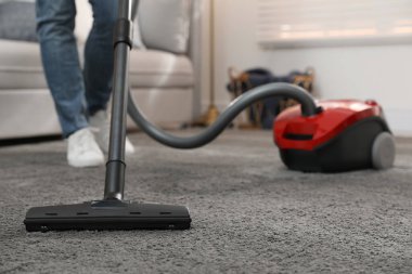 Evde elektrikli süpürge kullanan genç adam, yakın plan.