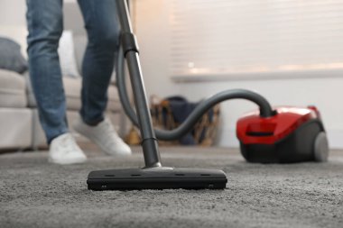 Evde elektrikli süpürge kullanan genç adam, yakın plan.
