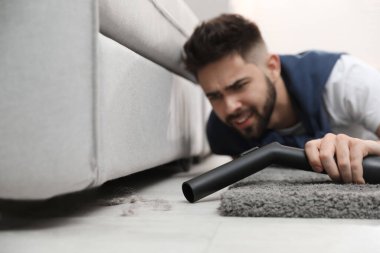 Evde elektrikli süpürge kullanan genç bir adam.