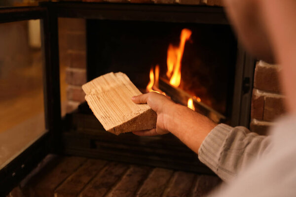 Man putting dry firewood into fireplace at home, closeup. Winter vacation