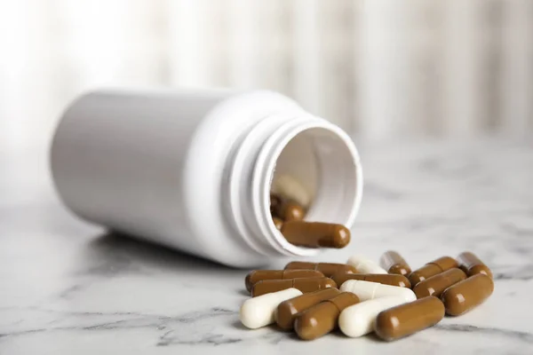 Bottle with vitamin pills on white marble table, closeup