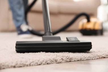 Evde elektrikli süpürge kullanan genç adam, yakın plan.