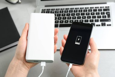 Cep telefonunu elektrik bankasıyla yükleyen kadın açık gri taş masada, yakın plan.