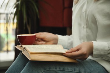 Elinde kahve fincanı olan kadın kitap okuyor, yakın plan.