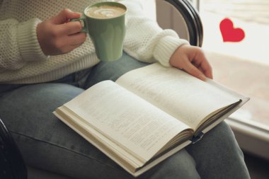 Elinde kahve fincanı olan kadın kitap okuyor, yakın plan.