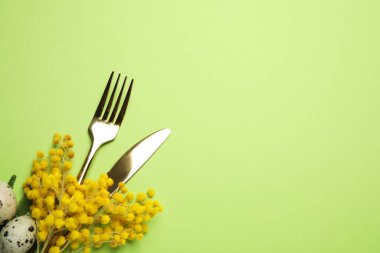 Yeşil arka planda bıldırcın yumurtası ve çiçek dekoru olan çatal bıçak seti seti, mesaj için yer. Paskalya kutlaması