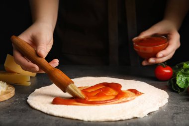 Gri masada pizza hamuruna domates sosu döken kadın, yakın plan.