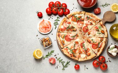 Lezzetli deniz ürünleri pizzası ve açık gri masada taze malzemeler.