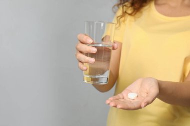 Açık gri arka planda bir bardak su ve vitamin hapı olan Afro-Amerikalı kadın, yakın plan. Metin için boşluk