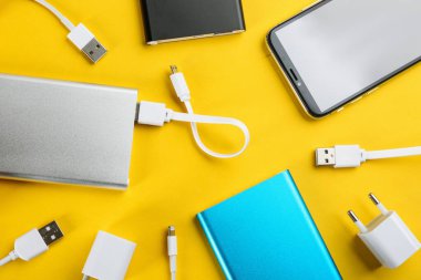 Mobile phone and portable chargers on yellow background, flat lay clipart