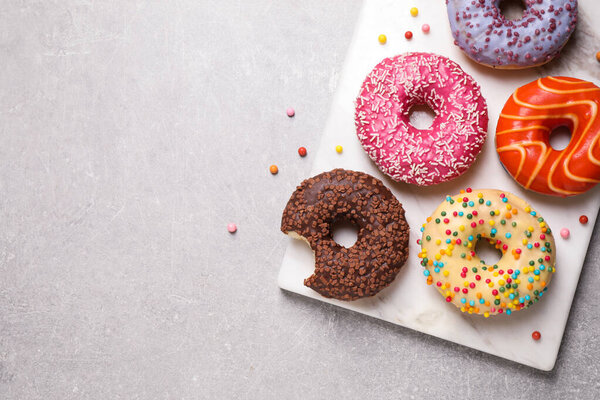 Yummy donuts with sprinkles on light grey table, top view. Space for text