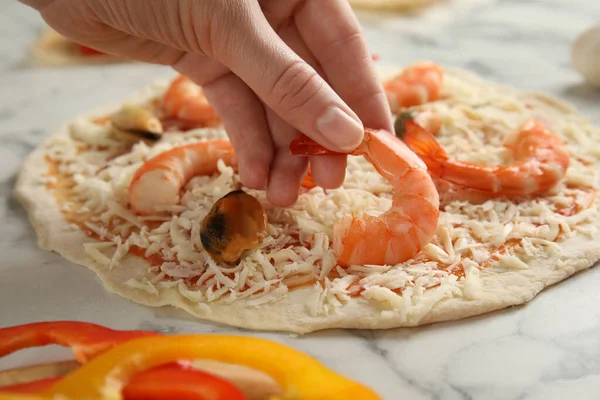 妇女在白色大理石桌旁的海鲜披萨中加入虾仁 — 图库照片