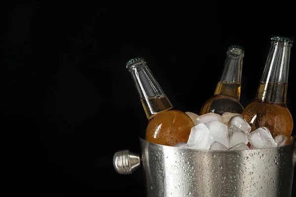 Metal bucket with bottles of beer and ice cubes on black background. Space for text