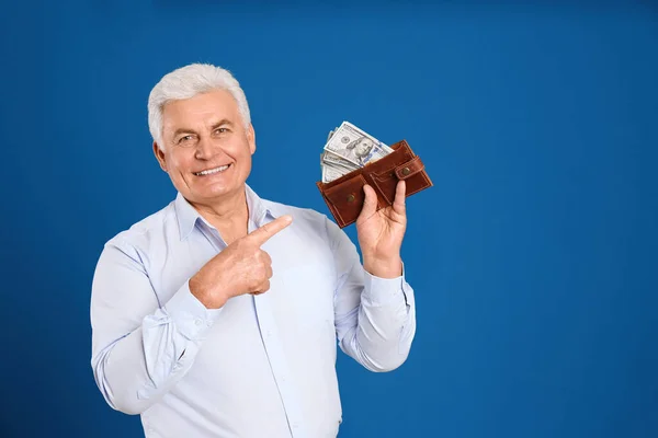Happy senior man with cash money and wallet on blue background