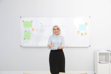 Modern sınıfta beyaz tahtanın yanında olgun bir öğretmen.