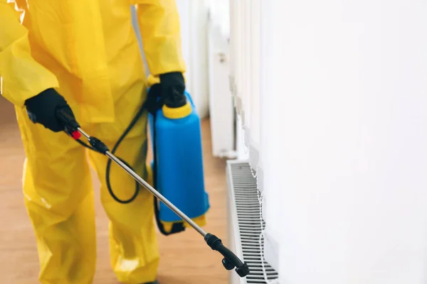 Pest control worker in protective suit spraying pesticide indoors, closeup. Space for text