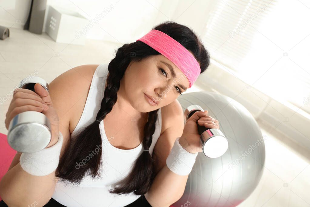 Lazy overweight woman with dumbbells at gym