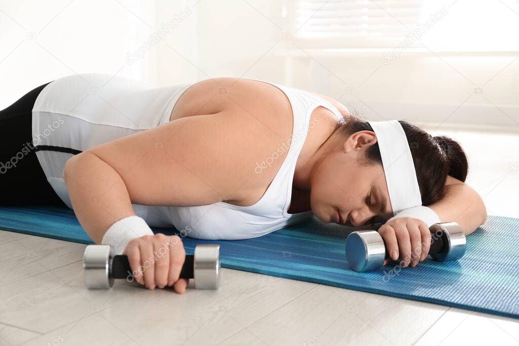 Lazy overweight woman with dumbbells sleeping on mat instead of training at gym