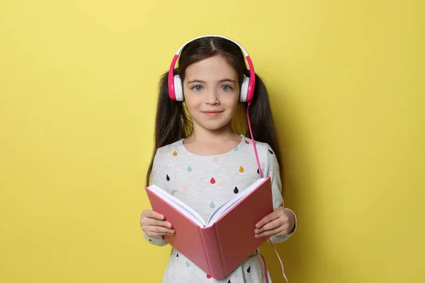 Cute Little Girl Słuchawkami Słuchając Audiobook Żółtym Tle — Zdjęcie stockowe