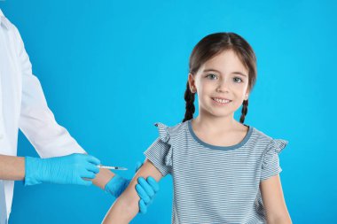 Açık mavi arka planda küçük bir çocuğu aşılayan doktor.