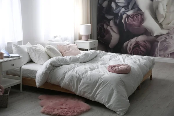 Comfortable bed near wall with floral wallpaper. Stylish room interior