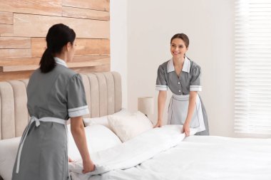Genç oda hizmetçileri otel odasında yatak yapıyor.