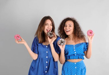 Açık gri arka planda donutları olan güzel genç kadınlar.