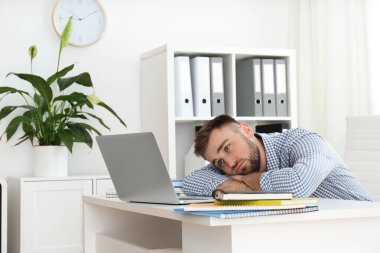 Lazy young man wasting time at table in office clipart