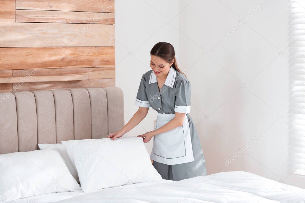 Young chambermaid making bed in hotel room