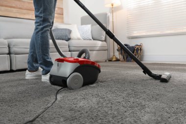 Evde elektrikli süpürge kullanan genç adam, yakın plan.