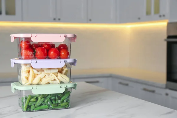 Containers with different frozen vegetables on white marble table in kitchen. Space for text