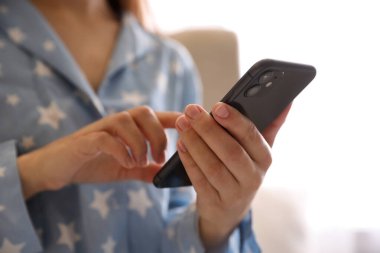 MYKOLAIV, UKRAINE - 16 Mart 2020: iPhone 11 'i açık arkaplanda tutan pijamalı kadın, yakın plan