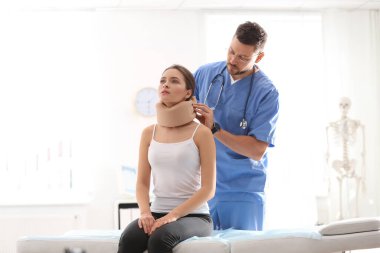 Erkek ortopedist klinikteki hastanın boynuna boyun tasması takıyor.