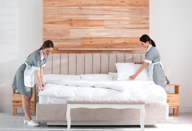 Genç oda hizmetçileri otel odasında yatak yapıyor.