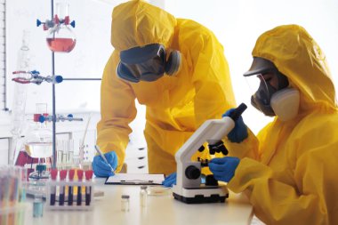 Laboratuvarda çalışan kimyasal koruyucu giysiler giyen bilim adamları. Virüs araştırması