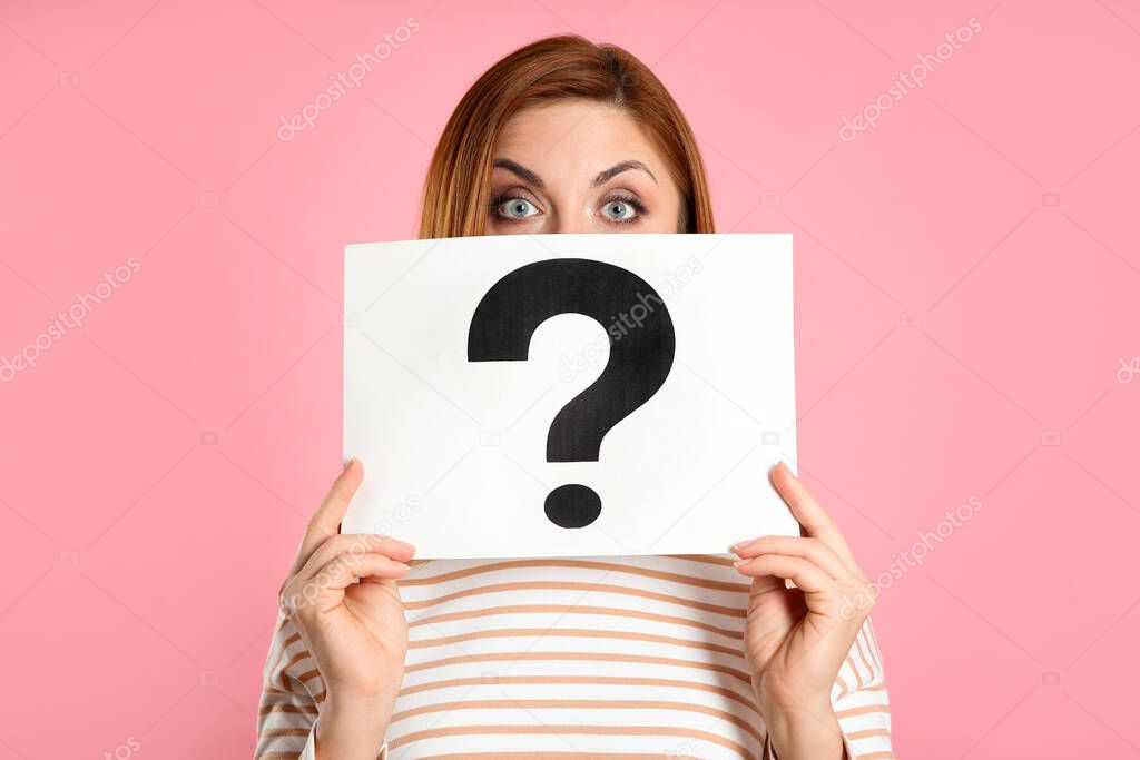 Emotional woman holding question mark sign on pink background