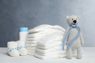 Bebek bezi, patik, şişe ve oyuncak ayı beyaz ahşap masada gri arka planda