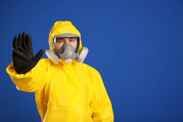 Man in chemical protective suit making stop gesture on blue background, space for text. Virus research