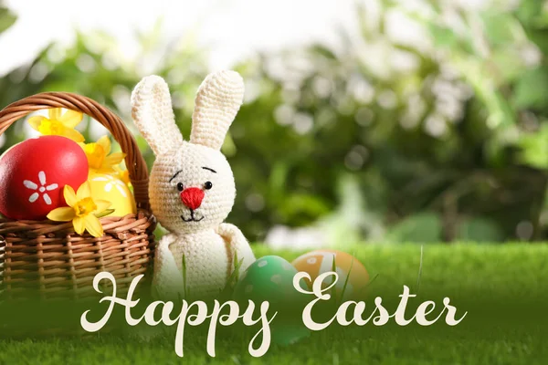 Colorful eggs, toy rabbit on green grass with text Happy Easter