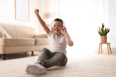 Küçük çocuk evde yerde müzik dinliyor.