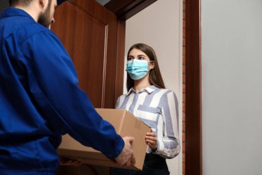 Tıbbi maske takan genç bir kadın içeride teslimatçıdan paket alıyor. Virüsün yayılmasını önlemek
