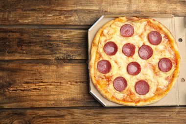 Tahta masadaki karton kutuda nefis pepperoni pizza, üst manzara. Metin için boşluk